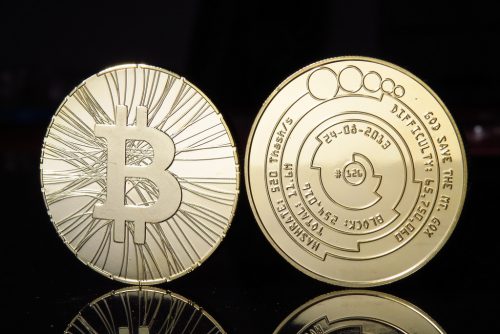 Zwei goldene Bitcoins stehen auf einer schwarzen spiegelnden Fläche.