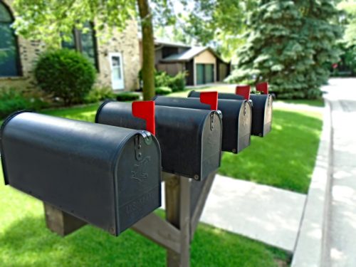Vier Briefkästen mit aufgestelltem Brief-Fänchen im Vordergrund einer Reihe von Hauseinfahrten