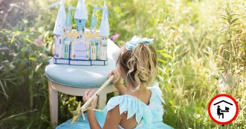 Ein kleines Mädchen sitzt als Prinzessin verkleidet auf einer Wiese und kehrt dem Betrachtenden den Rücken zu. Vor ihr steht ein Hocker auf dem ein kleines Schloss steht.