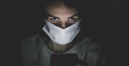 Person schaut verschwörerisch ins Smartphone und trägt dabei eine Atemschutzmaske.